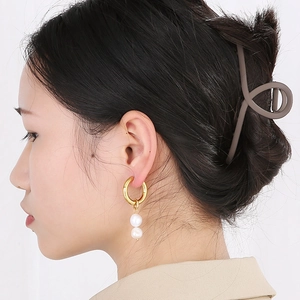 Détail de boucles d'oreilles perles dorées et d'une pince à cheveux mate sur un mannequin