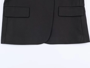 Detail of black blazer featuring flap pockets and rounded hem on smooth fabric