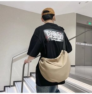 Rear view of model wearing a beige crossbody half-moon bag on modern indoor stairs