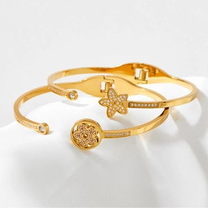 Gold stainless steel star and flower bracelets with pavé crystals on white fabric