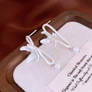 Macro detail of matte white lily flower earrings with elegant faux pearl pendants