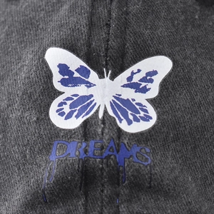 Casquette en coton délavé avec papillon brodé et texte Dreams bleu style graffiti