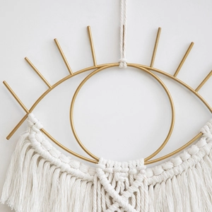 Close-up of golden metal eye macrame wall hanging with intricate cotton fringe details