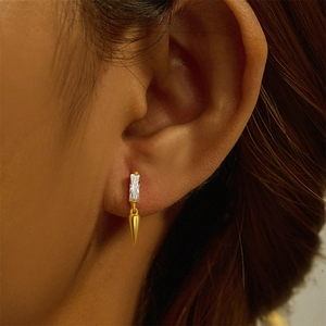 Close-up of golden stud earring with a rectangular clear gem and cone-shaped pendant charm