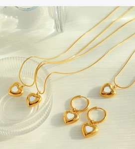 Detailed view of gold heart jewelry set with white shell inlay on textured fabric