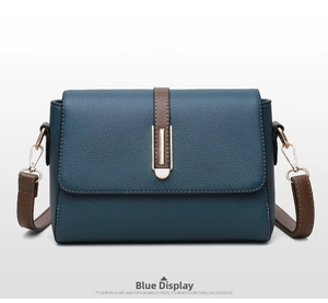 Detail of blue square crossbody bag with textured leather, gold metal bar, and brown strap