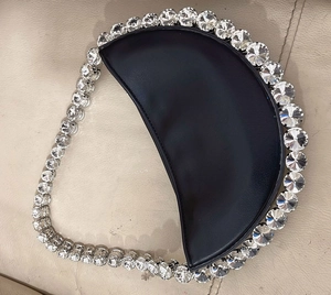 Macro detail of sparkling round rhinestones on a black crescent-shaped evening bag