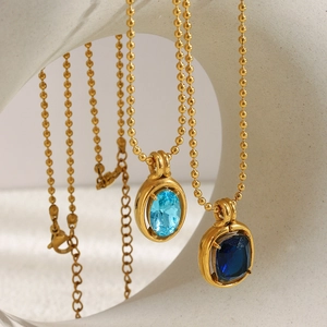 Macro detail of 18K gold-plated bead chains with blue zircon pendants on a white sculpture