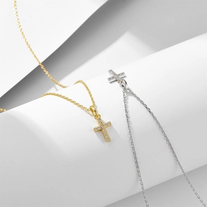 Minimalist silver and gold cross necklaces with sparkling diamonds on a white geometric stage