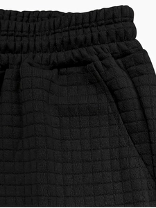 Detail view of black waffle textured sports shorts with elastic waistband and side pockets