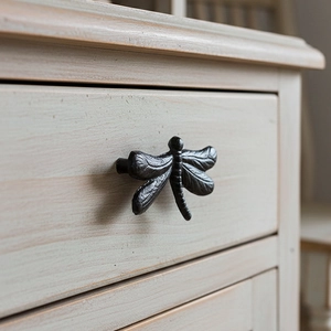 Vintage black iron dragonfly drawer pull handle mounted on a light wood cabinet drawer