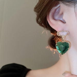 Detailed close-up of emerald green heart crystal earrings with pink zircon on model
