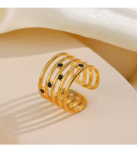 Detailed view of layered gold-tone ring with black beads on a beige texture surface