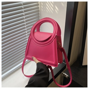 Detail of rose pink trapezoid handbag featuring unique round handle and matte leather finish