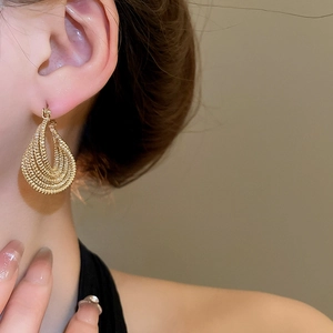 Close-up of a model wearing gold layered twisted oval drop earrings with a vintage finish
