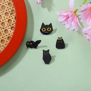 Detail view of four black enamel cat pins in various cute poses on a pastel green surface