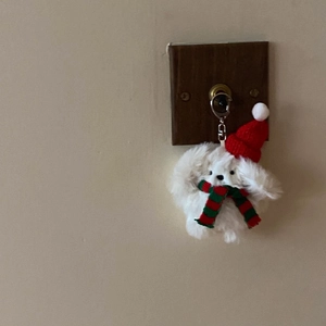 Close-up of white plush bunny keychain with red knit hat and striped scarf on wall hook