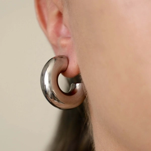 Macro shot of silver hollow hoop earrings in polished steel worn by a model