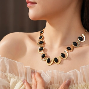 Détail d'un collier géométrique doré avec des pierres précieuses ovales noires sur modèle