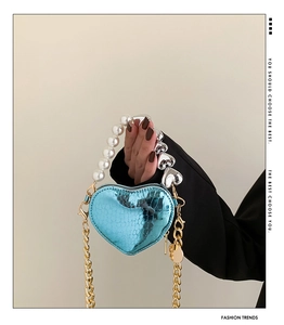 Détail du mini sac en forme de cœur avec poignée en perles et texture croco bleu