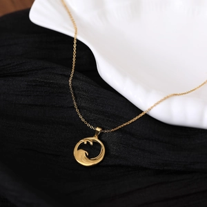 Gold stainless steel sun wave pendant necklace displayed on white shell over black fabric