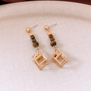 Detailed view of gold earrings featuring tiger eye beads and a creative chair pendant
