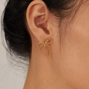 Minimalist gold bow-shaped stainless steel earring worn by a model in a close-up view