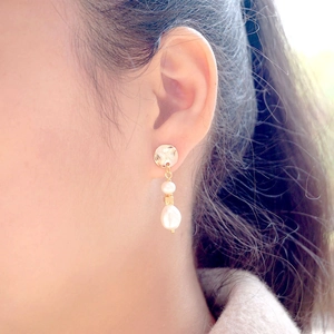 Elegant baroque pearl drop earrings with golden textured metal disc on female model