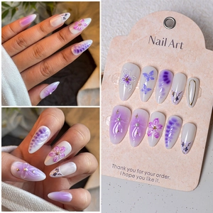 Detail of almond press-on nails with 3D purple flowers, butterfly designs and gold accents