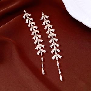 Detail of gold tassel earrings with zircon leaf studs on dark brown silk background