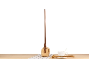 Detail of hand-woven straw crossbody bag with brown leather strap on wooden surface