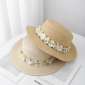 Detail of two boater straw hats with floral ribbon trim on a magazine background