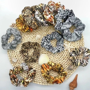 Detailed view of satin scrunchies with animal prints and shells on a woven mat