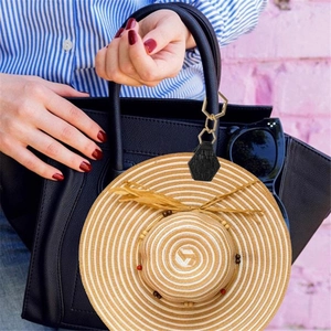 Detail of a black leather hexagonal hat clip with gold chain hanging on a handbag