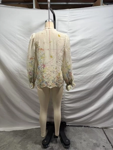 Detail view of floral embroidery and ruffled cuffs on back of apricot chiffon blouse