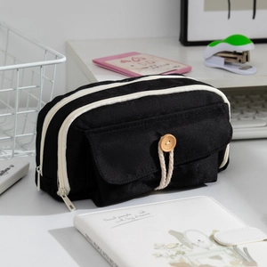 Black canvas pencil case with three zipper layers and wooden button detail on desk