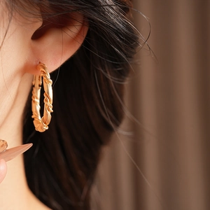 Close-up of elegant gold twisted hoop earrings worn by a model in soft lighting