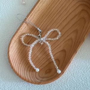 Detail of transparent acrylic bow phone charm with a metal star and pearl accents