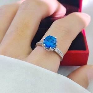 Detailed view of silver ring with 6-prong blue stone on finger and red box