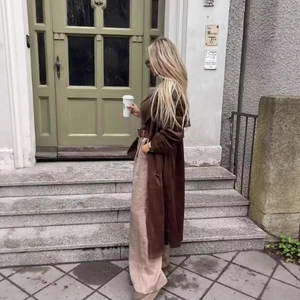 Elegant woman in brown trench coat and beige wide-leg trousers standing by a rustic door