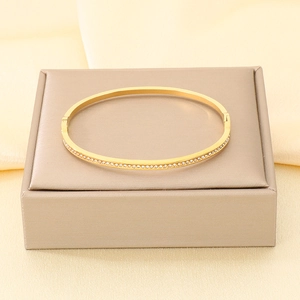 Primo piano di un elegante bracciale rigido in oro con accenti di cristallo pavé.