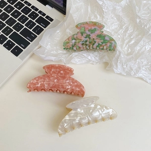 Trois grandes pinces à cheveux en acétate aux motifs marbrés et nacrés sur un bureau