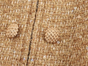 Detailed macro of golden tweed fabric with metallic threads, sequins and woven buttons