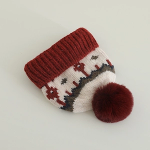 Dettaglio del berretto in maglia rosso e bianco con motivi ad albero e grande pompon