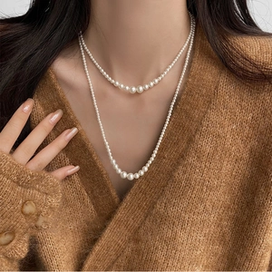 Close-up of elegant double-layered gradient pearl necklace on a beige knit sweater