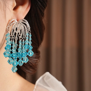 Close-up of blue faceted bead tassels hanging from silver curved metal earrings
