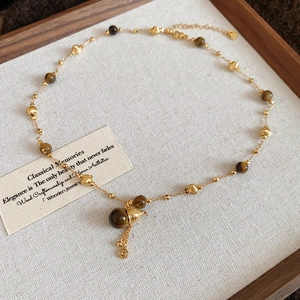 Detail of 18K gold plated tiger eye necklace with vintage tassel pendant on wood tray
