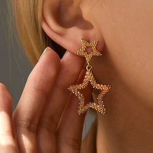 Detail of 18K gold plated double star earrings with textured grainy finish on model