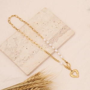 Golden heart pendant necklace with white pearls on a minimalist stone background