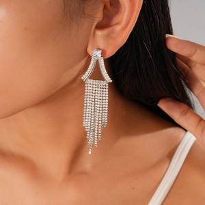 Détail de boucles d'oreilles pendantes argentées avec pompons et losanges diamantés